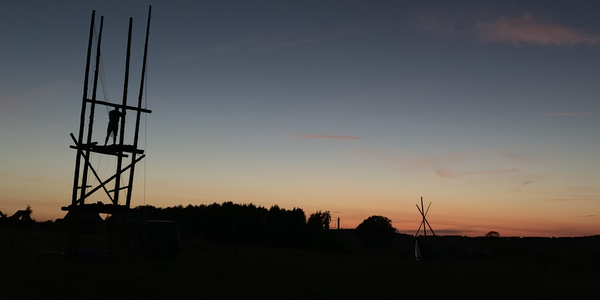 Une tour de pionniers en bois se découpe sur le ciel orange d’un coucher de soleil au camp